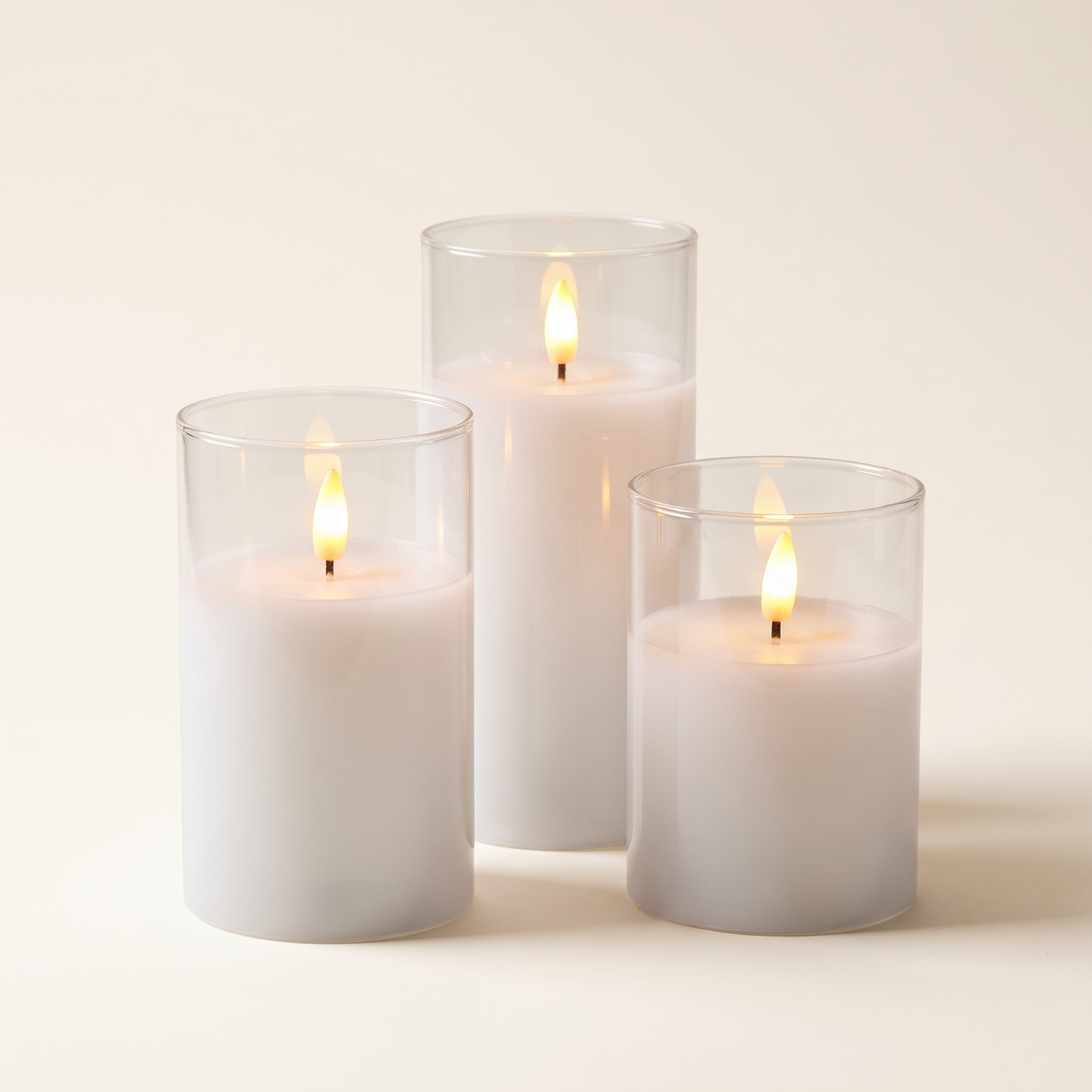 Set of three flameless LED candles in clear holders on a plain background
