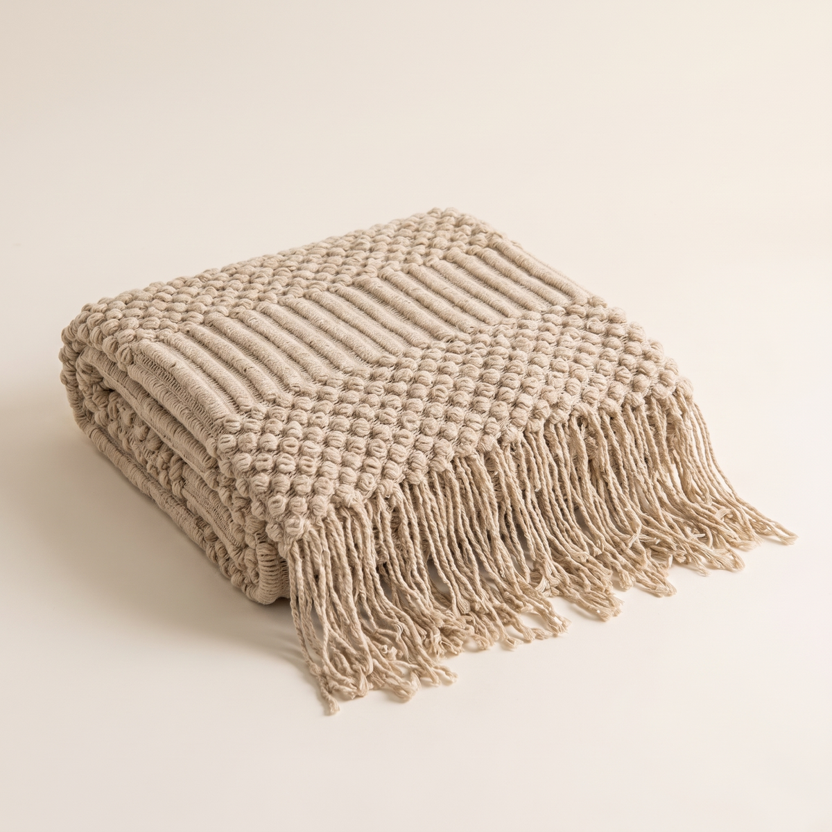 Folded khaki chunky knit throw blanket with tassels on a plain background