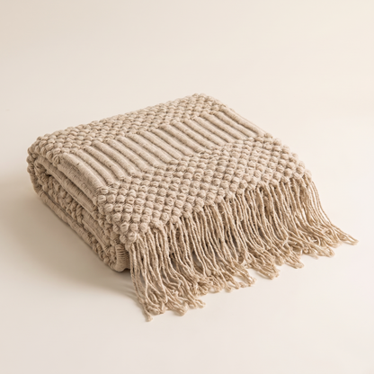 Folded khaki chunky knit throw blanket with tassels on a plain background