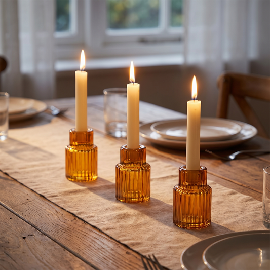 Three amber ribbed glass candle holders with lit candles on a dining table
