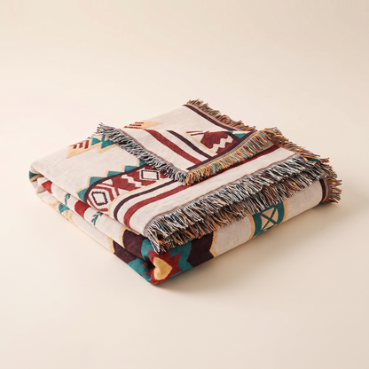 Folded boho woven throw blanket with fringe on a plain background