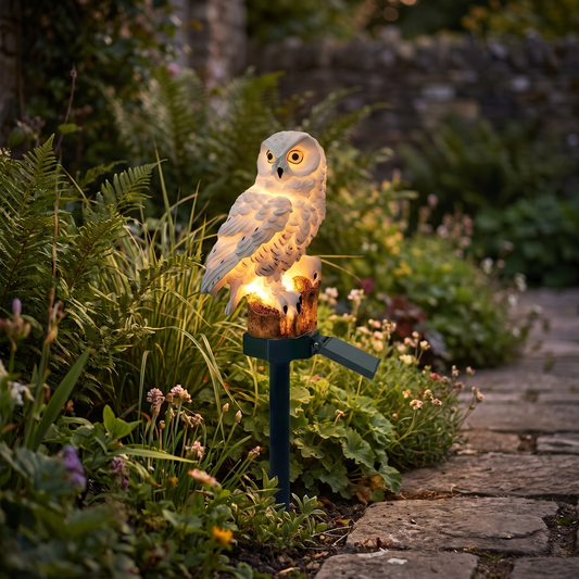 Solar owl garden light glowing in a garden border at dusk